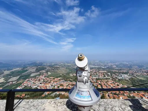 Telescopio con vista panoramica su cosa vedere a San Marino. Il paesaggio collinare e la città si estendono sotto un cielo azzurro con nuvole sottili.