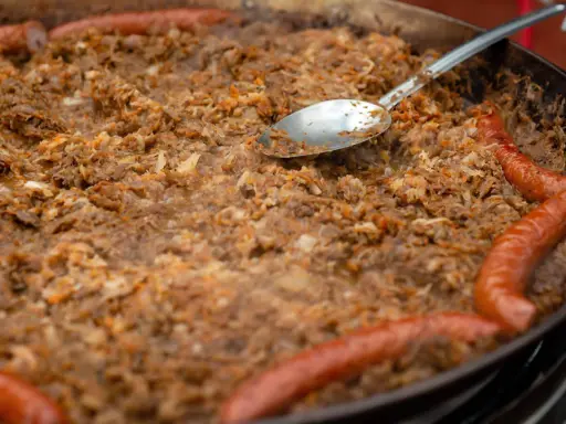 Wielki gar bigosu z kiełbasą, gotowy do wekowania w piekarniku. Łyżka zanurzona w aromatycznym daniu.