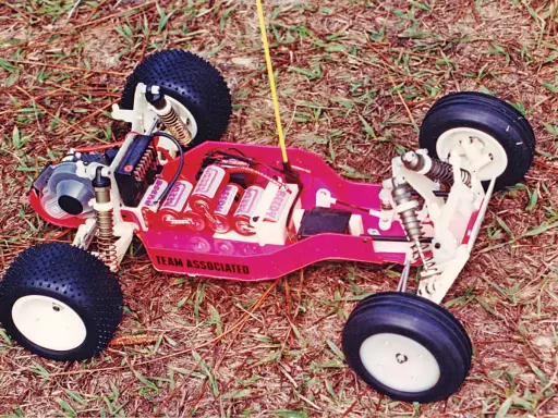 Ein ferngesteuertes Auto von Team Associated mit Batterien und Reifen auf Gras.