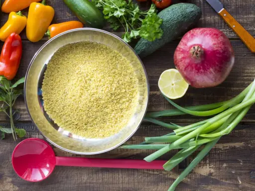 Schüssel mit Bulgur, einer tollen Quelle für **bulgur protein**, umgeben von frischem Gemüse wie Paprika, Gurken, Granatapfel und Frühlingszwiebeln.