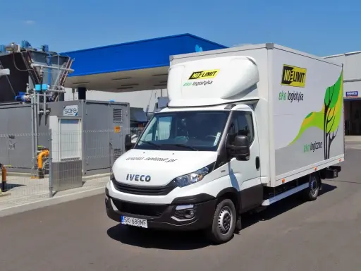 Biała ciężarówka Iveco zasilana gazem CNG, z logo "NO LIMIT eko logistyka", zaparkowana przy stacji paliw.