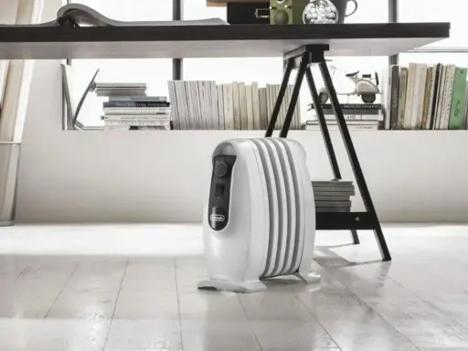 Un radiatore ad olio bianco, sotto una scrivania, mostra come funziona per riscaldare l'ambiente.