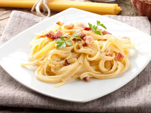 Pyszny makaron carbonara z boczkiem i natką pietruszki na białym talerzu.