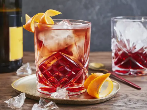 Ein erfrischender Negroni Sbagliato mit Eis und Orangenzeste, serviert auf einem goldenen Teller.