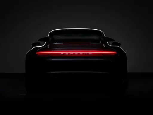Ein schwarzer Porsche von hinten, dessen Rückleuchten in einem leuchtenden Rot erstrahlen und den Schriftzug "PORSCHE" beleuchten.