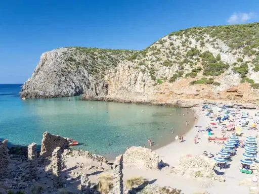Spiaggia affollata con ombrelloni colorati, acque cristalline e scogliere verdi. Perfetta per vacanze al mare economiche e rilassanti.