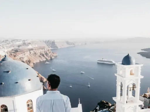 A man gazes at the caldera on a gay Greek island, with iconic blue domes and white architecture overlooking the Aegean Sea.