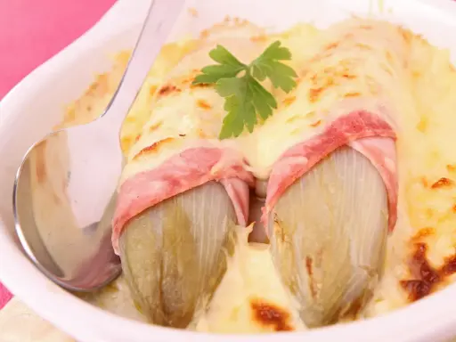 Deux endives braisées enveloppées de jambon, nappées de fromage fondu et gratiné, garnies d'une feuille de persil. Un plat réconfortant.
