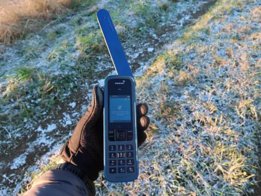 Ręka w rękawiczce trzyma telefon Inmarsat IsatPhone, gotowy do nawiązania połączenia przez telefonię satelitarną w mroźny poranek.