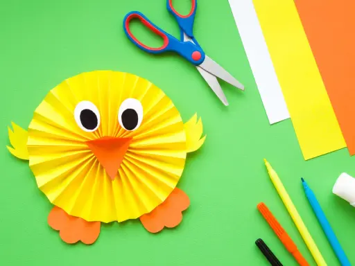 Manualidades para niña de 2 años: un pollito de papel. Tijeras, papeles de colores, rotuladores y pegamento listos para crear.