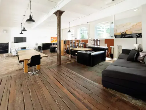 Geräumiges Loft mit Holzboden, großen Fenstern, Arbeitsbereich und gemütlicher Sitzecke. Eine perfekte loft definition.