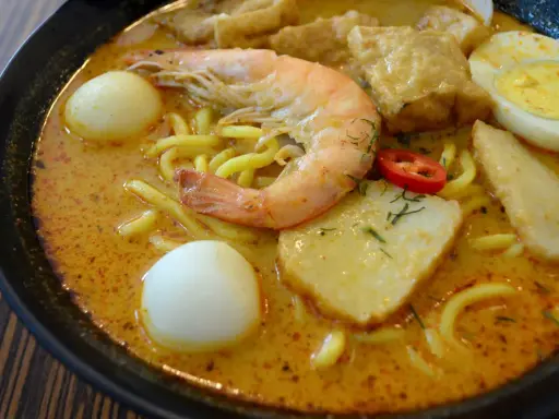 Eine Schüssel Laksa, ein beliebtes Singapur-Essen, mit Garnelen, Ei, Tofu und Nudeln in cremiger Kokosbrühe.