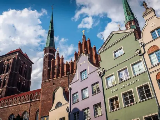 Kolorowe kamienice w Gdańsku pod błękitnym niebem z chmurami, w tle kościół.