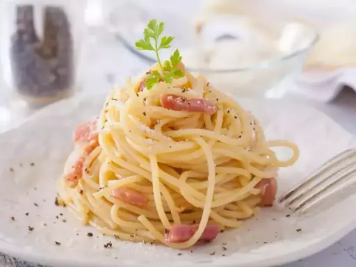 Un plat de tagliatelles carbonara crémeuses, garni de lardons et de persil frais, prêt à être dégusté.