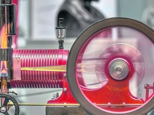 Eine funktionierende Denis Papin Dampfmaschine mit rot glühendem Kessel und einem sich drehenden Schwungrad.