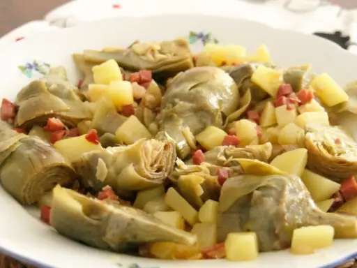 Plato de alcachofas tiernas y patatas cortadas en cubos, salpicado con trocitos de jamón. Un manjar casero.