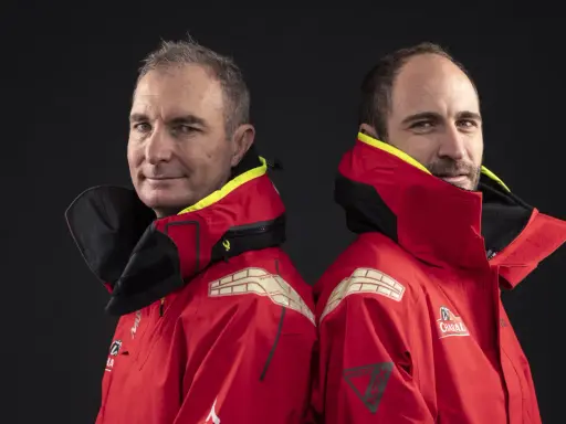 Morgan Lagravière et son coéquipier, deux marins en veste rouge, prêts pour l'aventure en mer.