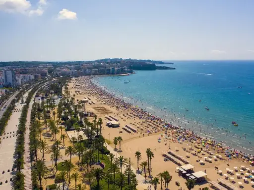 Tłum ludzi cieszy się słońcem na plaży, a w tle widać miasto. To idealne miejsce na wakacje, pełne atrakcji Costa Dorada.