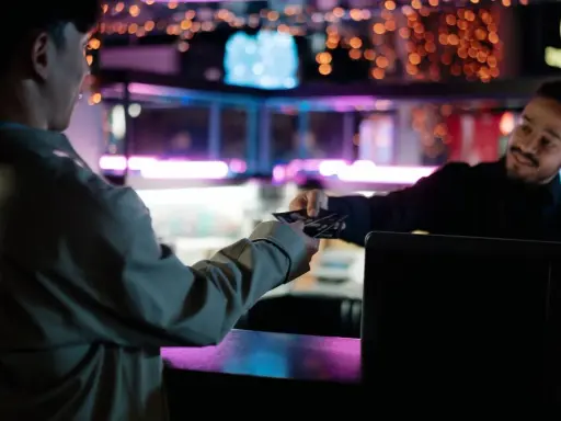 Un cliente entrega tarjetas a un camarero en un bar con luces de neón. Existe el derecho de admisión en los bares.