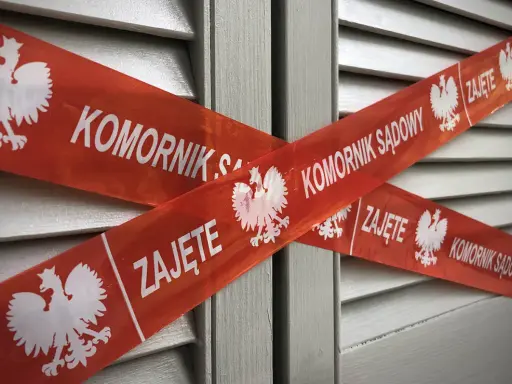 Czerwona taśma z napisem "KOMORNIK SĄDOWY" i godłem Polski krzyżuje się na szarej powierzchni. Jak pozbyć się komornika z konta?