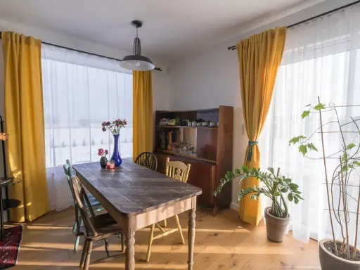 Słoneczne, żółte zasłony tworzą przytulny wystrój okien w stylu retro. Drewniany stół i kredens dodają ciepła.