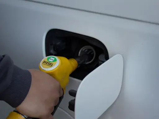 Ręka trzymająca żółtą dyszę dystrybutora, tankuje samochód. Na dyszy widnieje napis "DIESEL B10".