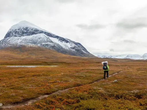 Vandrare på Kungsleden i Sarek med snöklädda berg i bakgrunden och höstens färger i förgrunden.