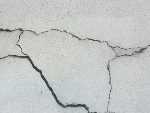 Pęknięcia na jasnej powierzchni betonu, świadczące o procesie karbonatyzacji.