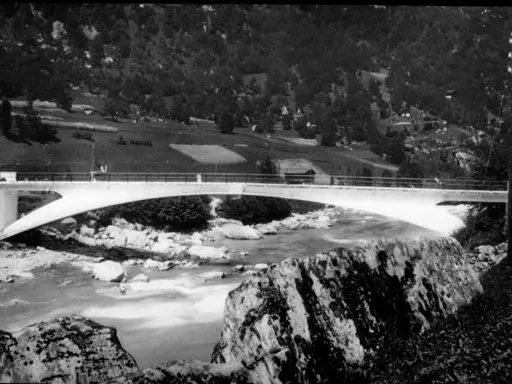 Puente de arco de hormigón de **Robert Maillart** sobre un río rocoso, con colinas boscosas al fondo.