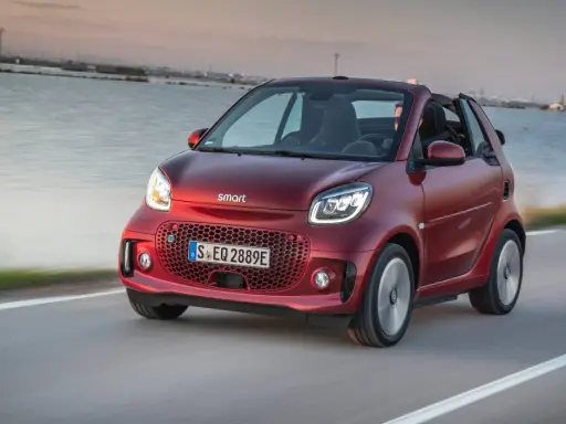 El Smart EQ Fortwo, cual es el coche más pequeño del mercado, se desplaza ágilmente por una carretera costera al atardecer.