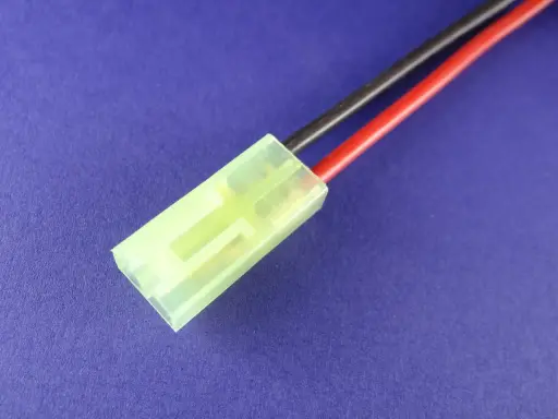 Ein gelber mini Tamiya Stecker mit roten und schwarzen Kabeln auf blauem Hintergrund.
