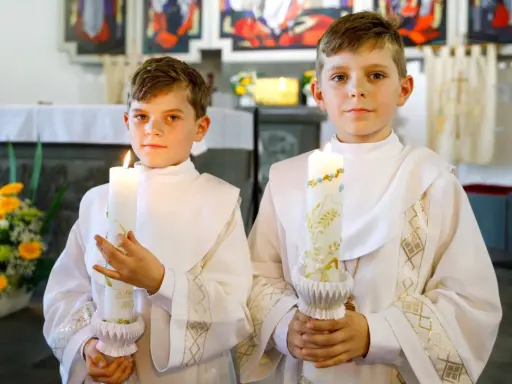 Dwóch chłopców w albach trzyma zapalone świece. Czy do komunii potrzebna jest świeca? Tak, symbolizuje światło Chrystusa.