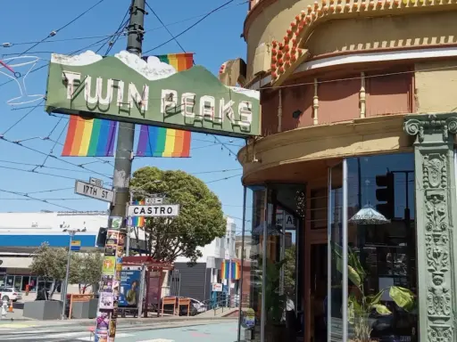 The iconic Twin Peaks sign hangs above Castro Street, a vibrant symbol of the gay area of San Francisco, adorned with rainbow flags.