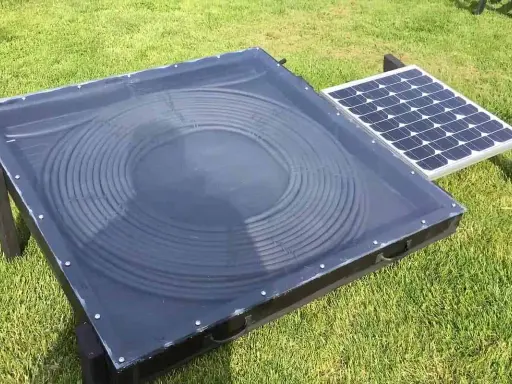 Un système de chauffage air solaire avec un panneau de tubes noirs en spirale sous une couverture transparente, à côté d'un petit panneau solaire.