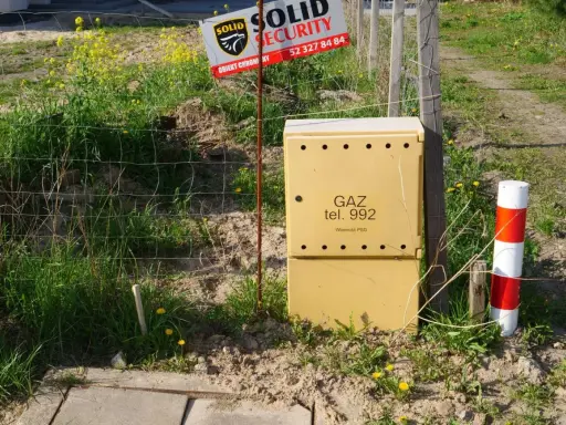 Żółta skrzynka gazowa z napisem "GAZ tel. 992" stoi obok ogrodzenia. Czy skrzynka gazowa musi być żółta?