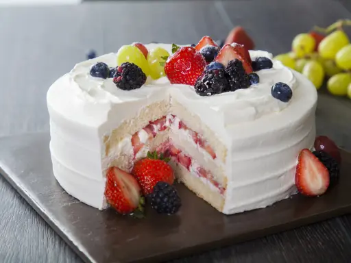 Pyszny tort z bitą śmietaną i mascarpone, przełożony truskawkami i owocami leśnymi. Udekorowany świeżymi owocami.
