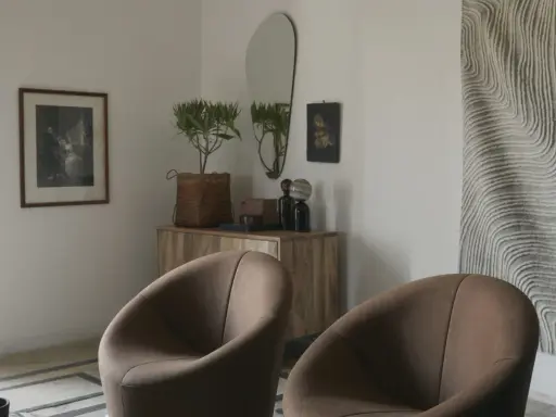 Två bruna fåtöljer framför en träbyrå med spegel och konst. En inredningsdröm inspirerad av Marie Olsson Nylander för Ellos.