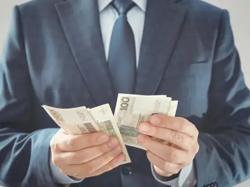 Mężczyzna w garniturze liczy banknoty 100 zł. To jego zabezpieczenie finansowe na przyszłość.