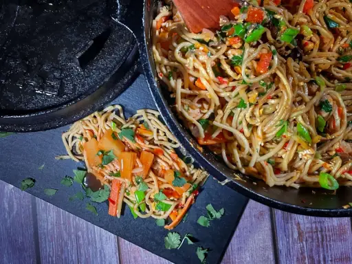 Leckere China Nudeln mit Gemüse und Kräutern werden aus einer Pfanne auf einen schwarzen Teller geschöpft.