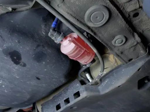 El filtro de combustible, de color rojo y transparente, está ubicado debajo del coche, cerca del tanque.