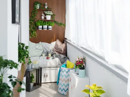 Przytulna loggia w bloku z wygodną kanapą, ziołami na półkach i bukietem kwiatów. Idealne miejsce na relaks.