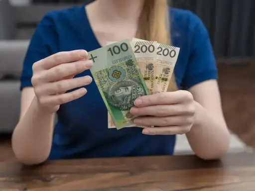 Kobieta trzyma polskie banknoty 100 i 200 zł. Zastanawia się, urlop macierzyński ile płatny.