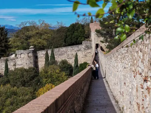 Spaziergang auf der Stadtmauer von Girona, Spanien. Zwei Frauen genießen die Aussicht auf die historische Festung und die grüne Landschaft.