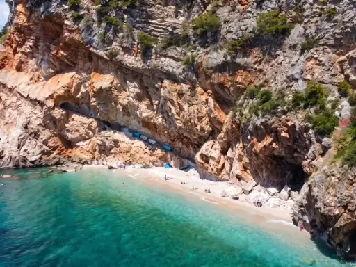 Versteckter geheimtipp kroatien strand: Eine kleine Bucht mit türkisfarbenem Wasser, umgeben von steilen Felsen. Einige Boote liegen am Ufer, wenige Menschen genießen die Ruhe.