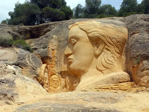 En la ruta de las esculturas, rostros emergen de la roca. Una gran cabeza femenina domina la escena, flanqueada por figuras más pequeñas.