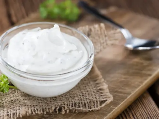 Una ciotola di panna acida cremosa, perfetta per la tua prossima ricetta. Un cucchiaino e un rametto di prezzemolo completano la scena rustica.