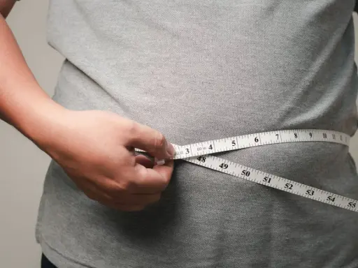 Eine Hand misst mit einem Maßband die Taille. Viele fragen sich, wo nimmt man zuerst ab – oft ist es der Bauch.