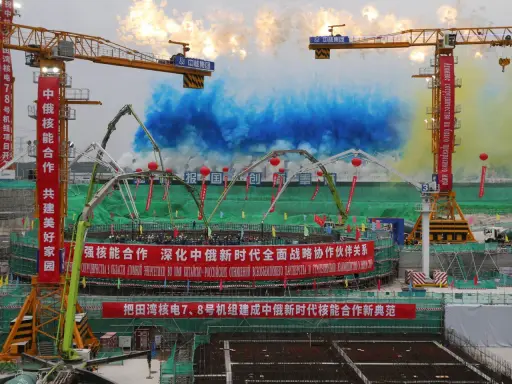 Bau von China Atomkraft-Anlagen mit Kränen und bunten Rauchsäulen. Chinesische und russische Banner feiern die Zusammenarbeit.