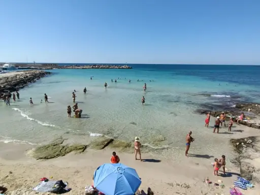 Gente in spiaggia e in mare vicino alla torre vado lungomare. Acqua cristallina e cielo azzurro.