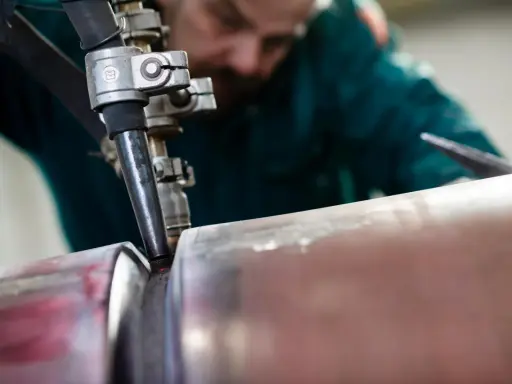 Saldatore esperto esegue saldatura ad arco sommerso su un tubo metallico, creando un giunto robusto.